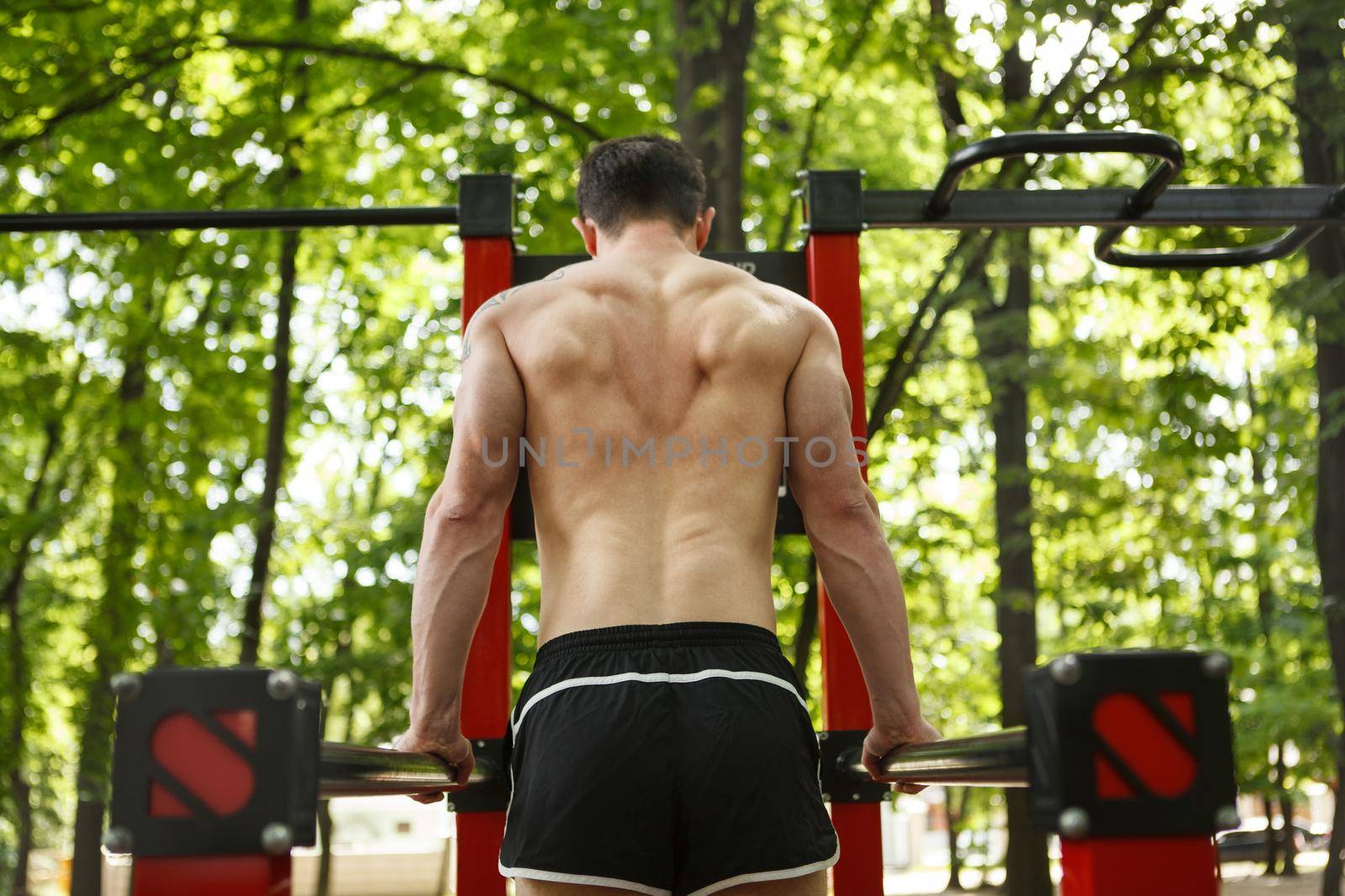 Rear view shot of an athlete with muscular back exercising on calisthenics playground