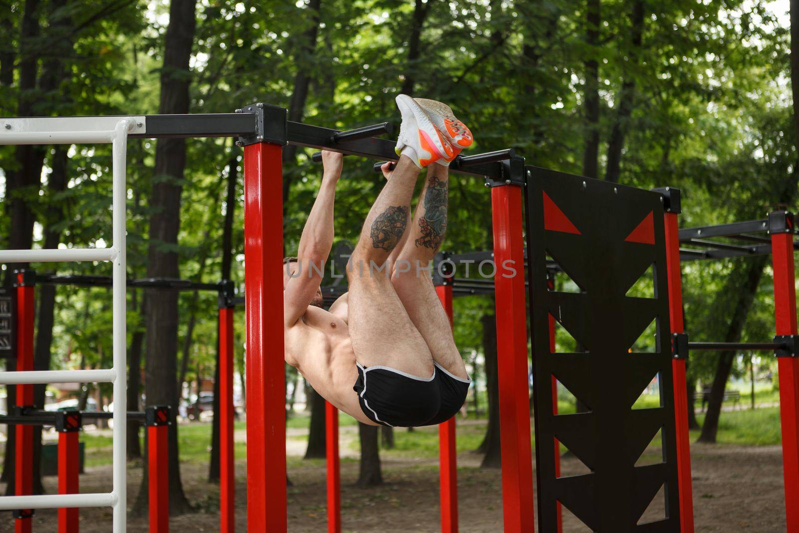 Strong sportsman doing toes to bar abdominal exercise outdoors