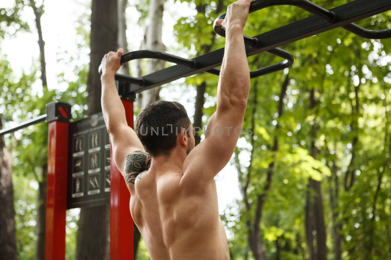 Cropped shot of an athletic muscular man doing pull ups on calisthenics workout playground