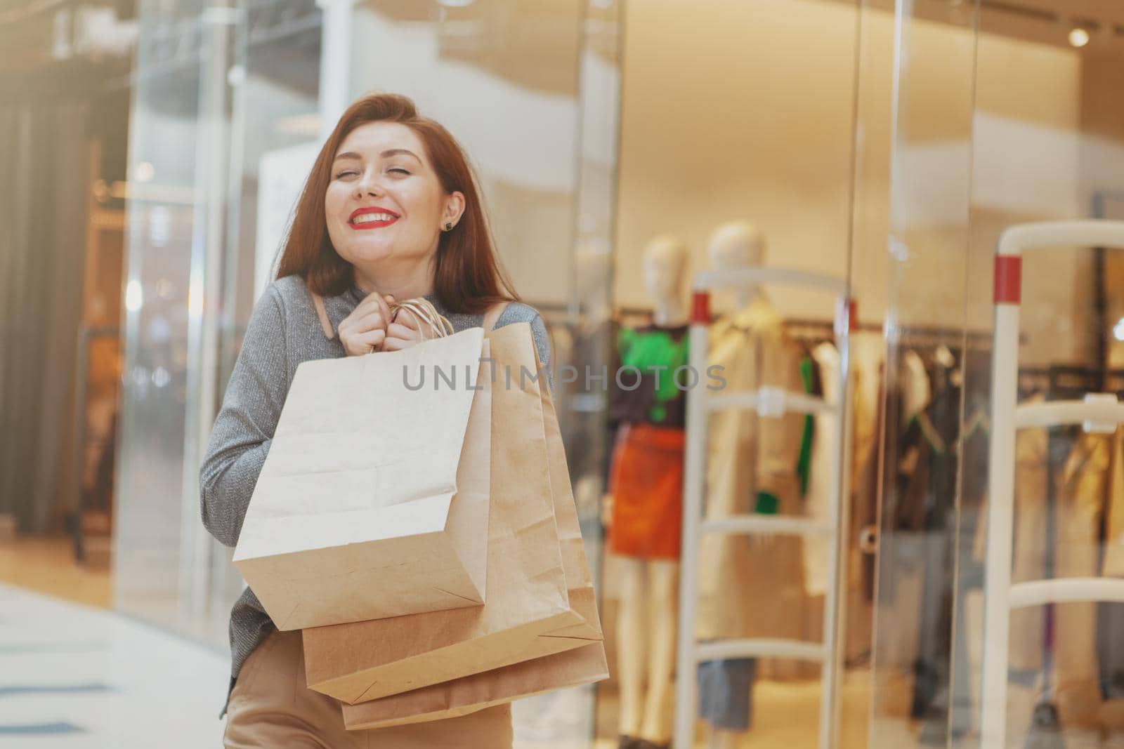 Excited young beautiful woman smiling with her eyes closed in pleasure, carrying her shopping bags at the mall. Extremely happy female customer at the shopping mall, copy space
