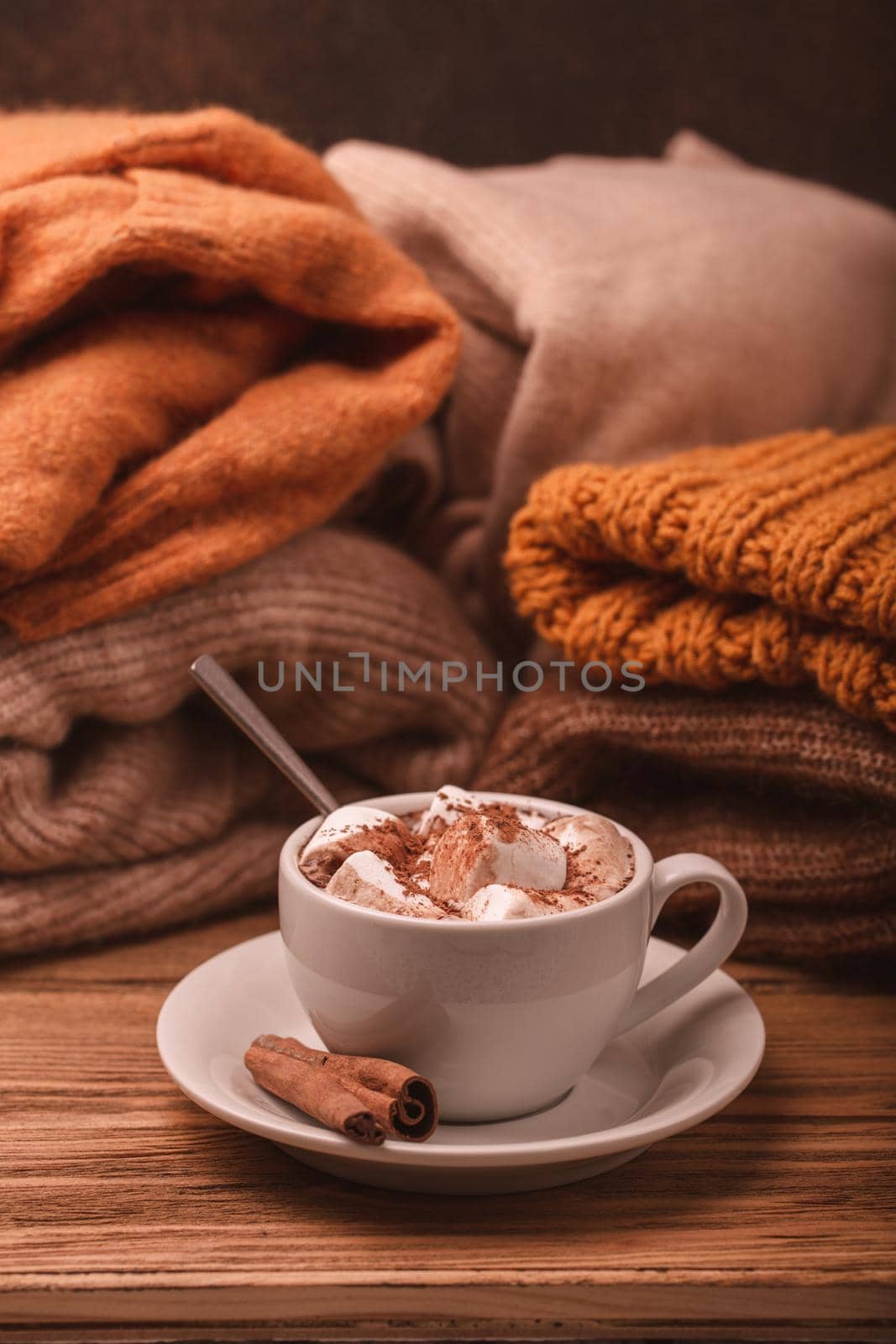 Cozy winter composition, cup with hot chocolate or cocoa with marshmallow and pile of warm knitted clothes on wooden rustic background. Comfy and soft winter at home, winter or autumn concept