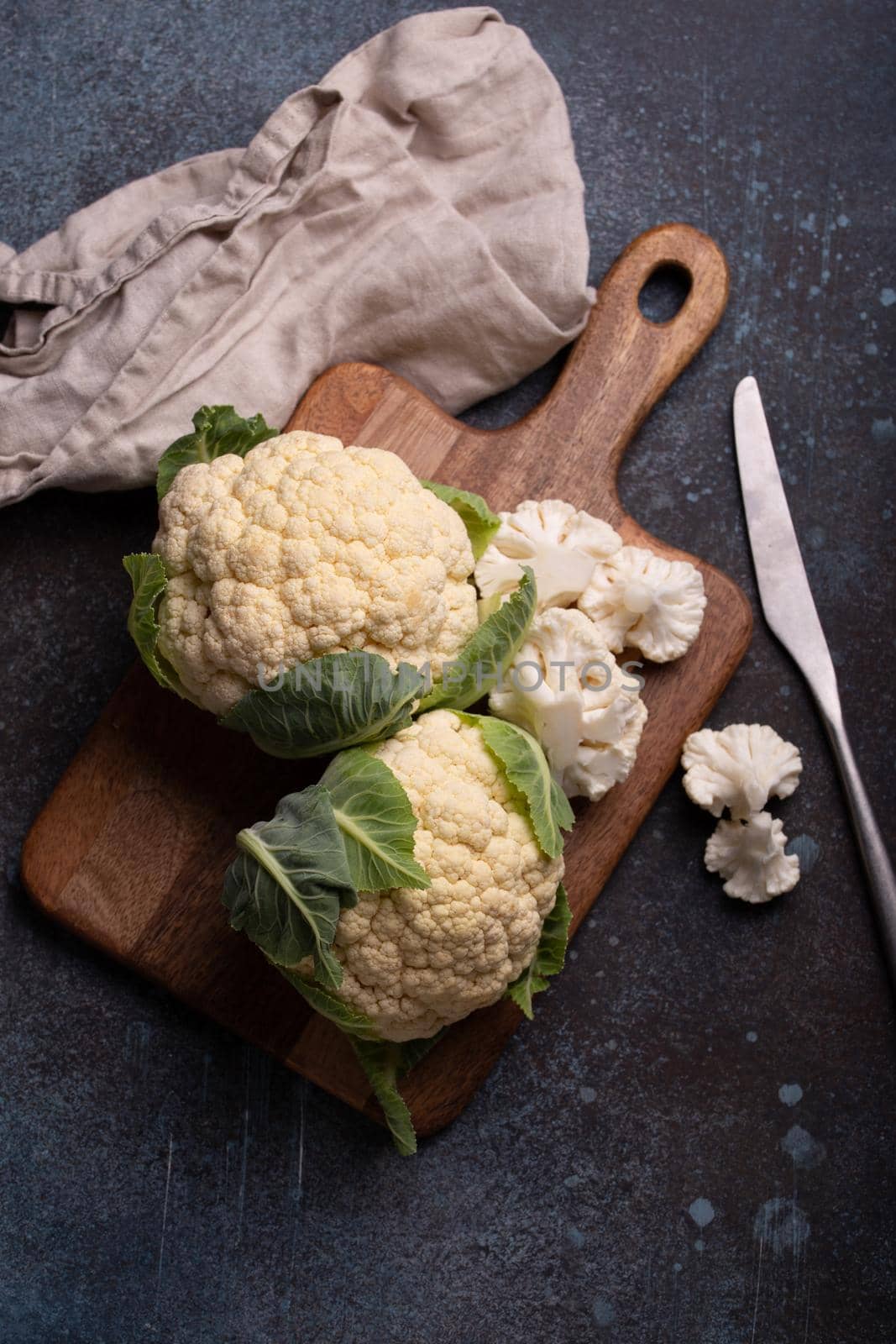 Fresh organic cut cauliflower on wooden cutting board with kitchen knife, ready to be cooked, top view with copy space. Vegetarian food, clean eating concept .