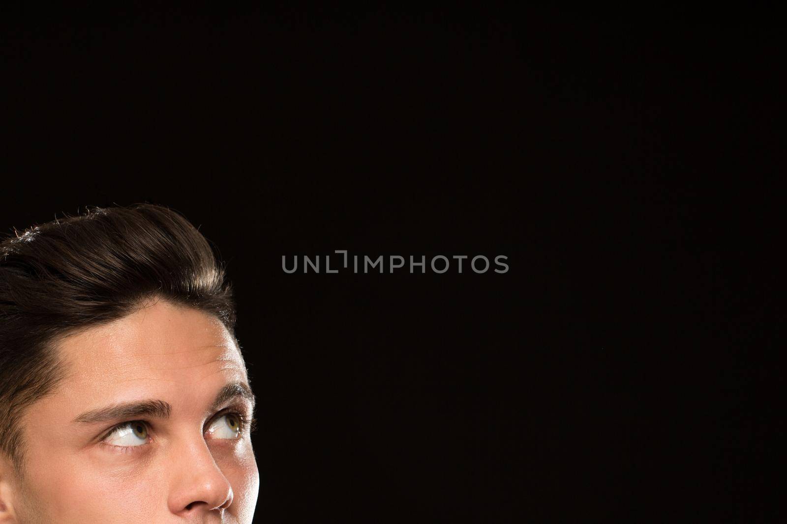 Cropped close up of a handsome young man with classy hairstyle looking at the copyspace on black background eyes half face emotions news ads expressive barbershop barber