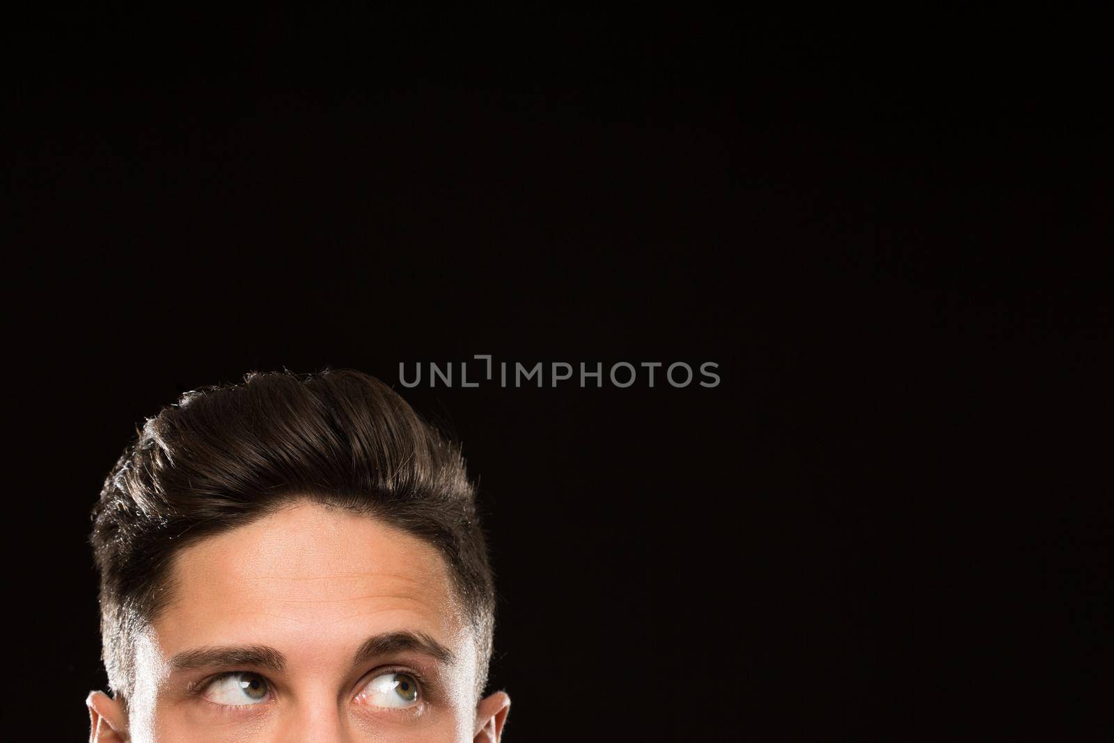 Cropped shot of a young man eyes on black background. Handsome man looking thoughtfully at the copyspace above his head hal face eye expressive hairstyle hair concept