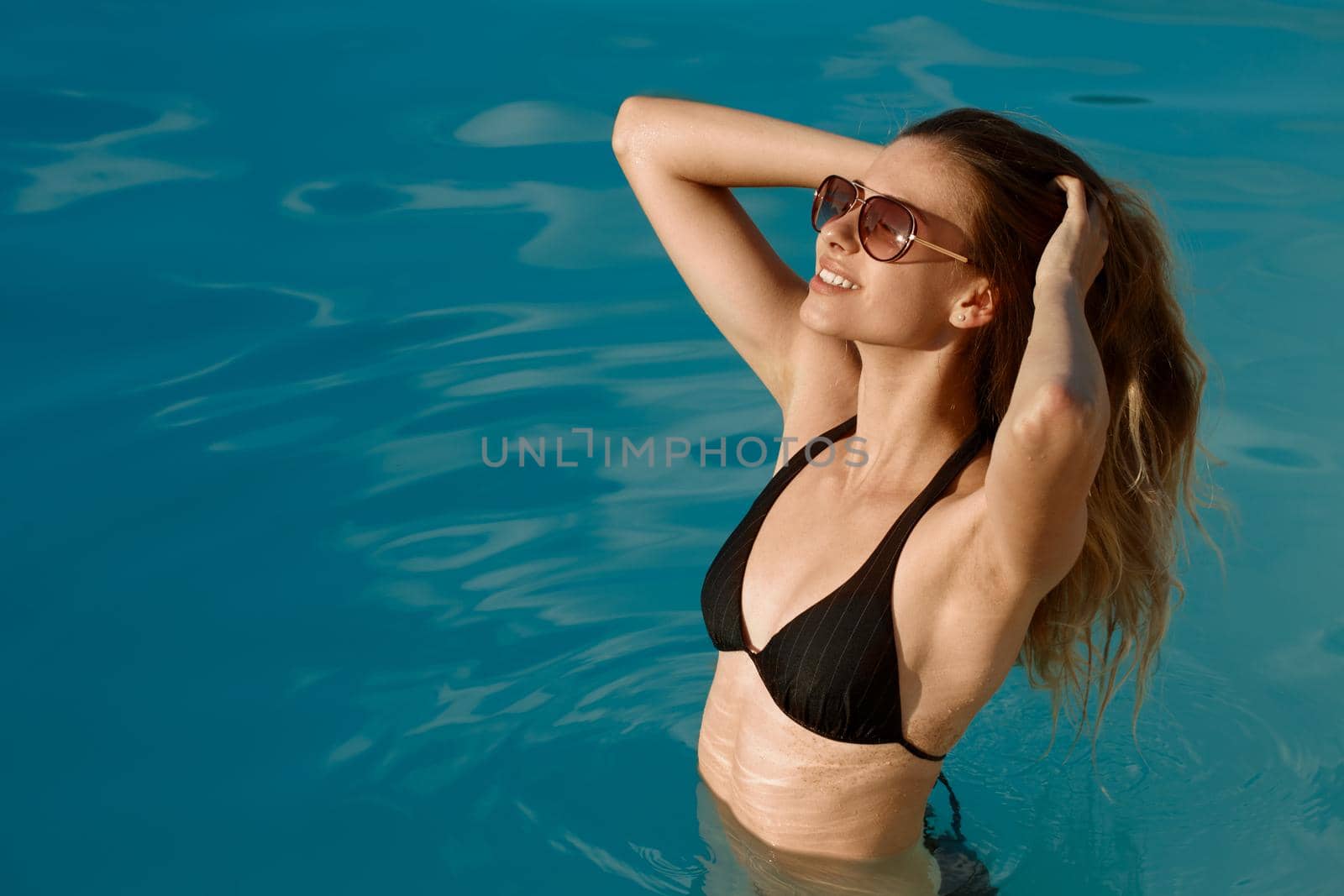 Gorgeous young woman enjoying a swim at the pool, copy space. Beautiful happy woman smiling, touching her hair sensually while relaxing at the swimming pool. Hotel, resort, vcation concept