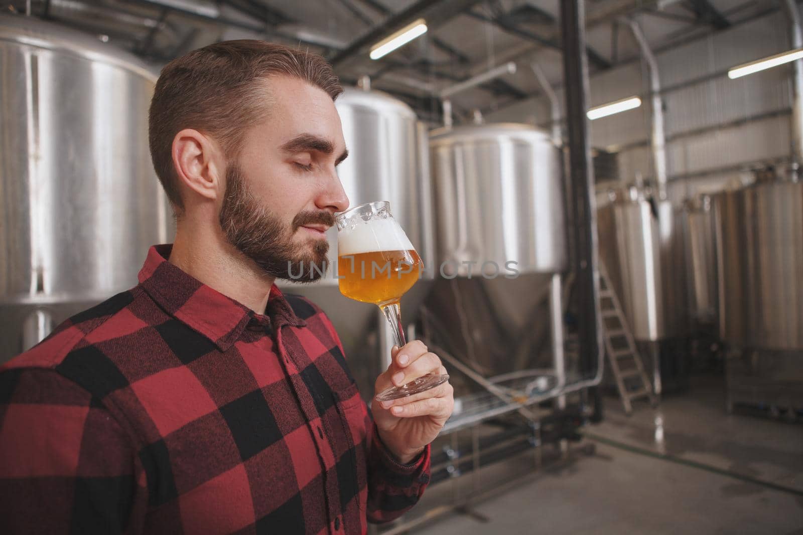 Handsome brewer examining freshly brewed beer at his beer factory by MAD_Production