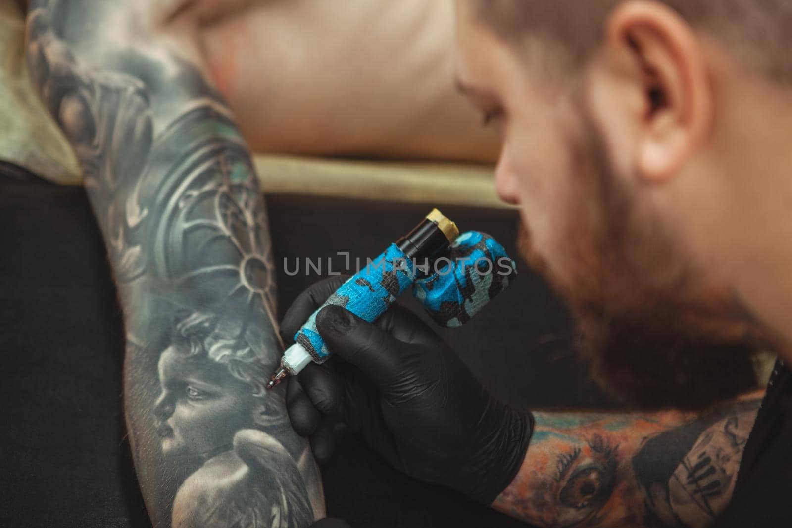 Bearded tattooist making tattoos on body of his client by MAD_Production