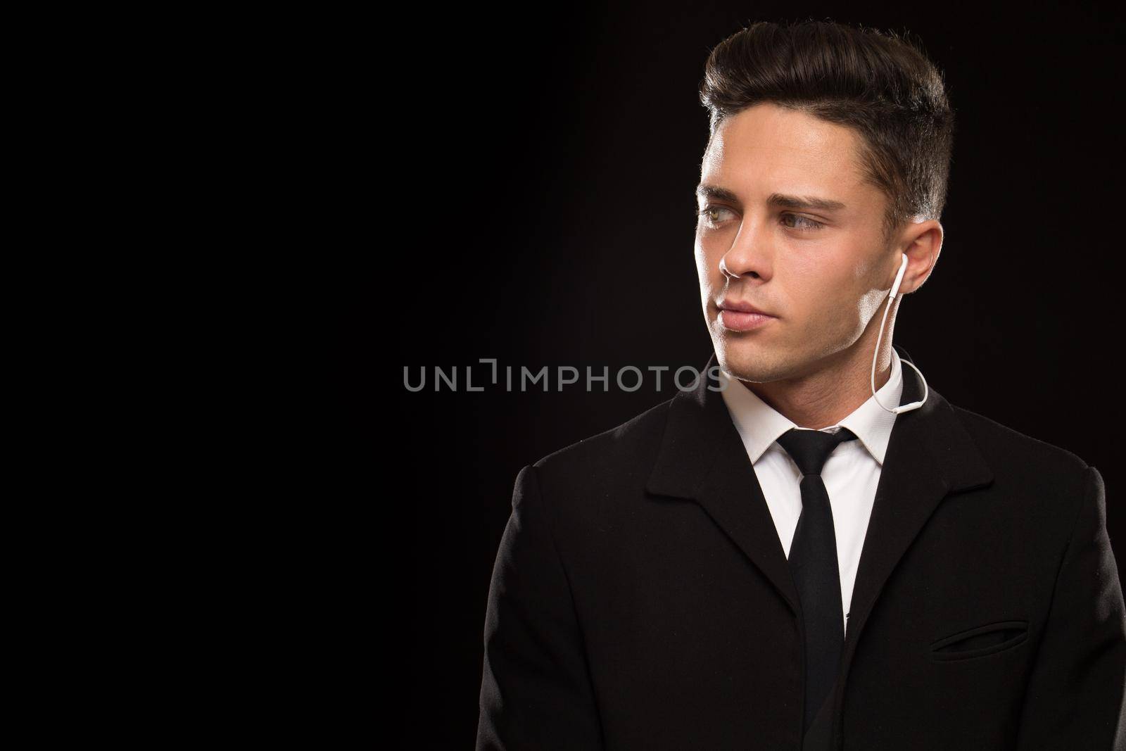 Handsome young professional bodyguard looking suspiciously at the copyspace on the side black background suspicion tension guard FBI secret agent profession job danger protective tense