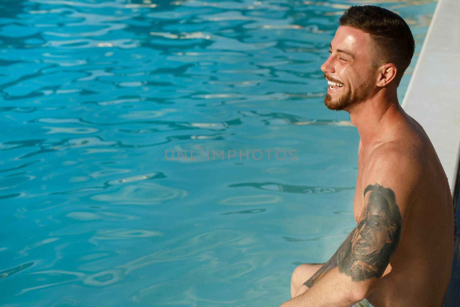 Cropped shot of a handsome happy man smiling with his eyes closed relaxing at the poolside, tanning on the sun, copy space. Handsome bearded man enjoying sunny summer day at the swimming pool