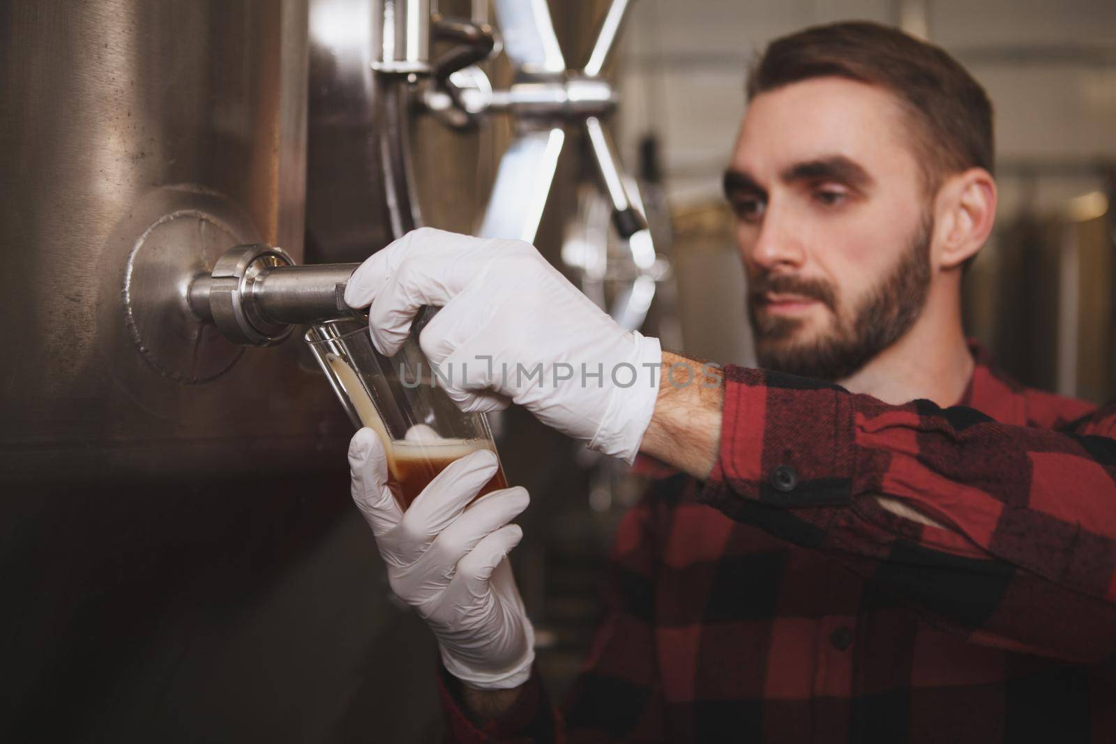 Professional brewer pouring beer into glass from beer tank at his brewery