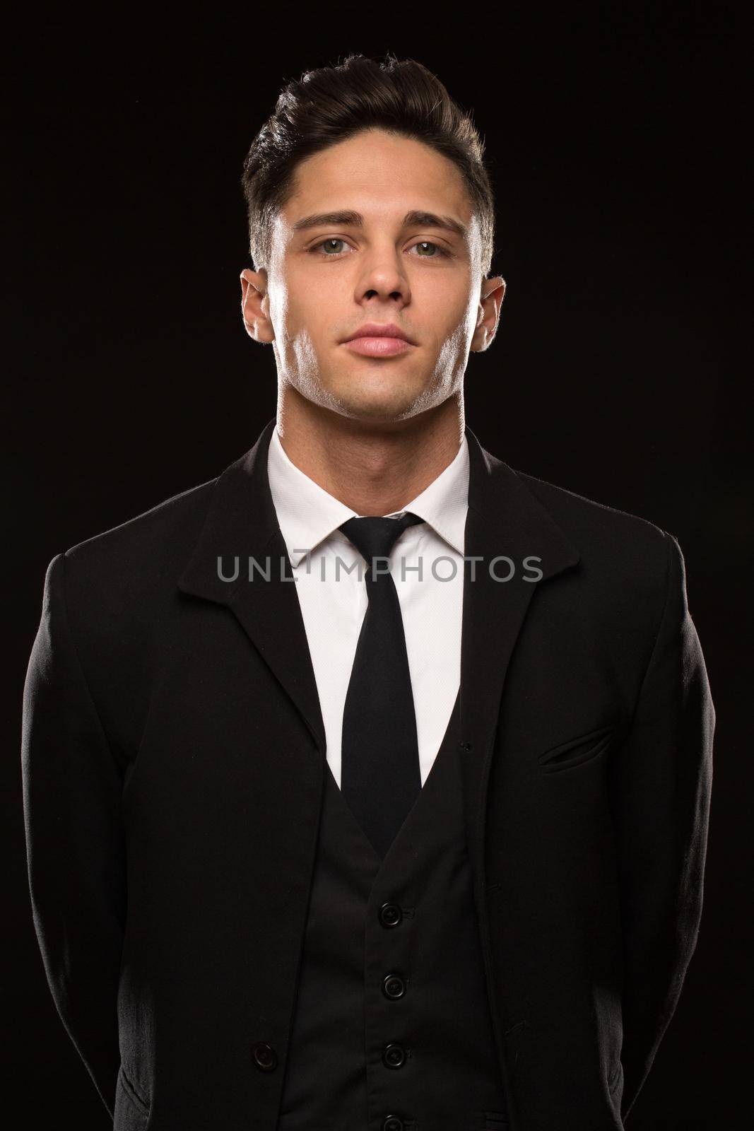 Vertical studio portrait of a handsome young secret service agent wearing black suit and a tie posing fiercely and confidently on black background safety bodyguard profession masculinity fearless