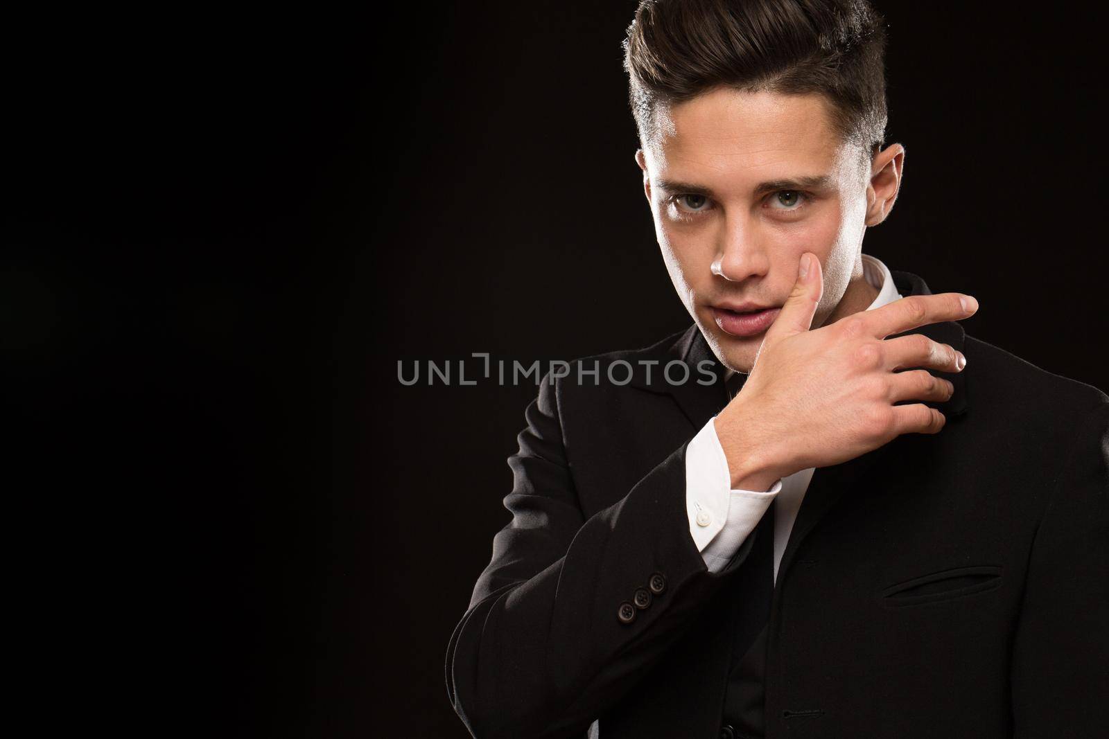 Studio shot of a sexy handsome suited young macho man looking aggressively to the camera wiping his face copyspace gesture brutal masculine seductive tempting epressive emotional secret agent