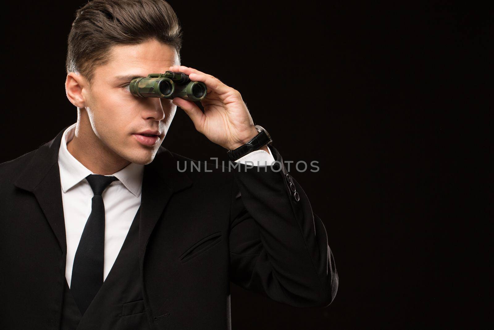 Close up shot of a handsome professional secret service agent looking away using binoculars on black background copyspace watching spy spying safety chasing FBI suspect searching search