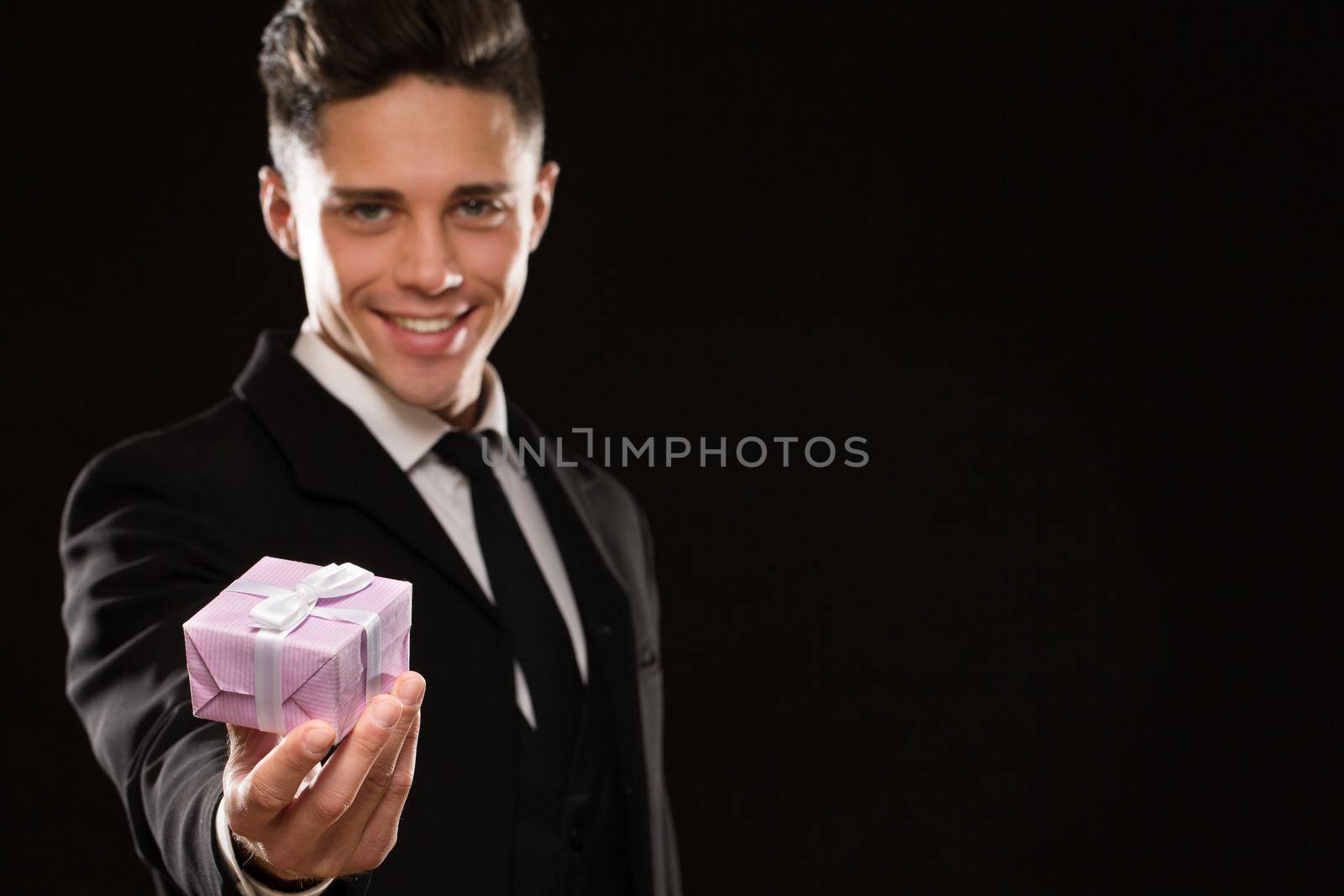 Selective focus on a present in the hand of a sexy handsome young man in an elegant classic suit copyspace black background anniversary romance gift celebration congratulating husband