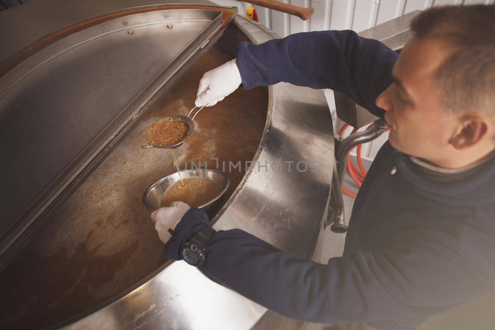 Top view shot of a man working at beer factory, examining fermenting beer in a tank