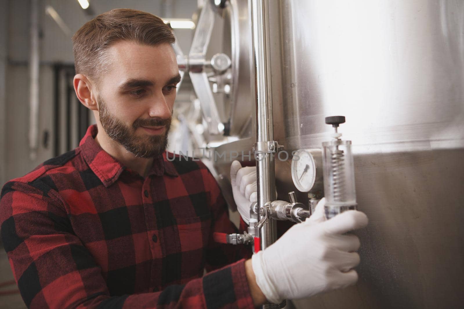 Attractive male brewer examining equipment at his beer factory