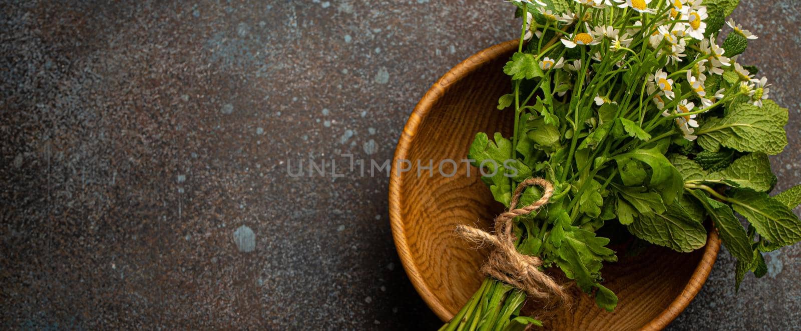 Bunch bouquet of fresh wild flowers and healing herbs in rustic wooden bowl top view flat lay on stone background for herbal alternative medicine and homeopathy, natural herbs medicine concept