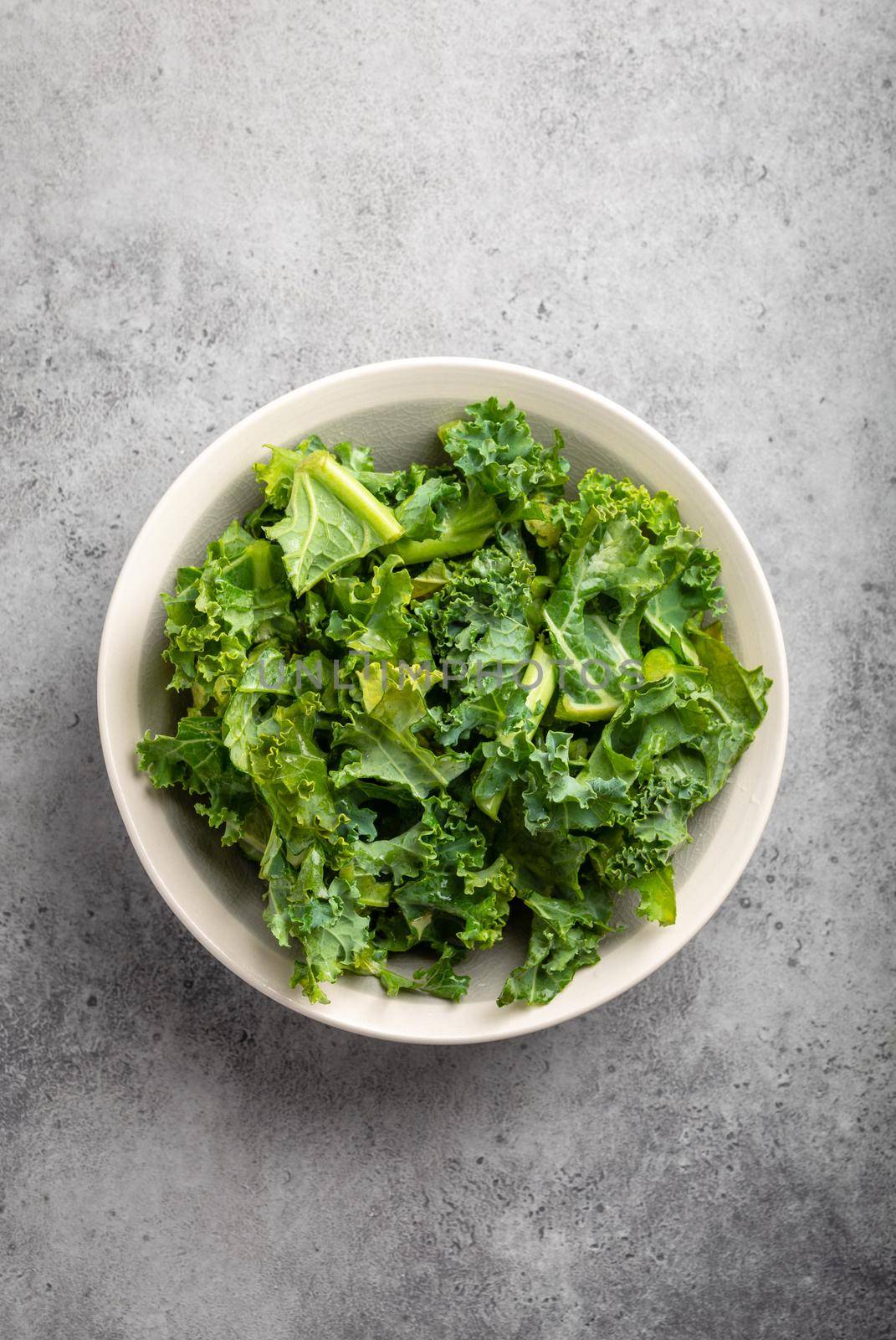 Bowl of fresh green chopped kale on gray rustic stone background, top view, close-up. Ingredient for making healthy salad. Clean eating, detox or diet concept