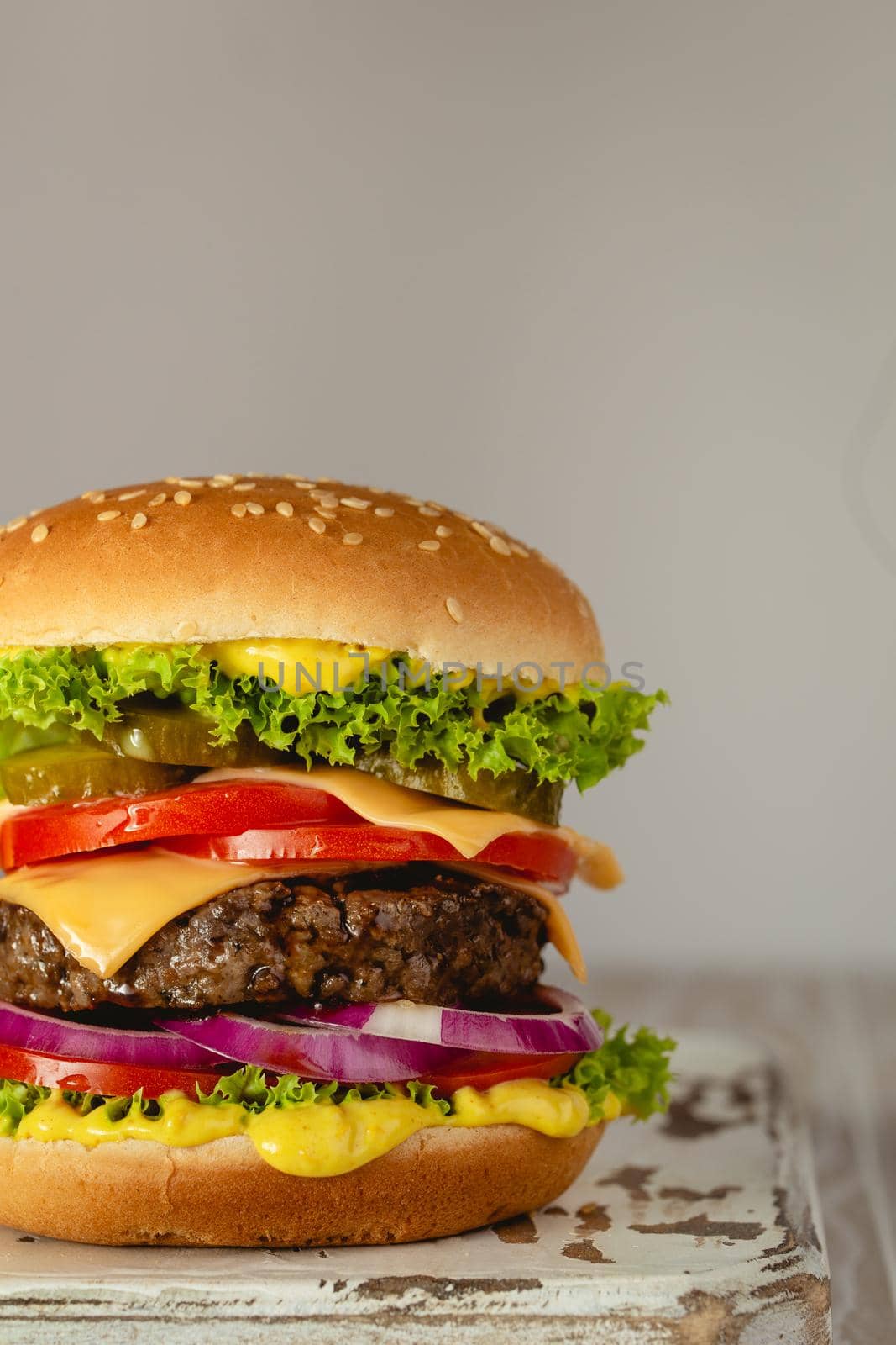 Delicious burger with meat, melted cheese, dripping sauce and vegetables on white rustic background. Freshly made tasty hamburger, close-up.