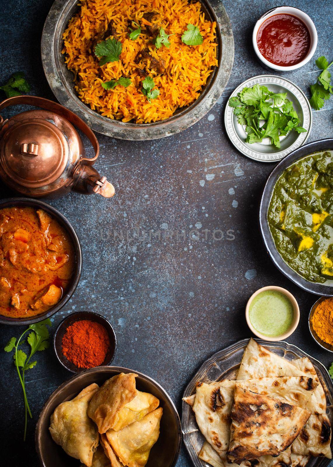 Overhead of Indian traditional dishes and appetizers: chicken curry, pilaf, naan bread, samosas, paneer, chutney on rustic background. Table with choice of food of Indian cuisine, space for text