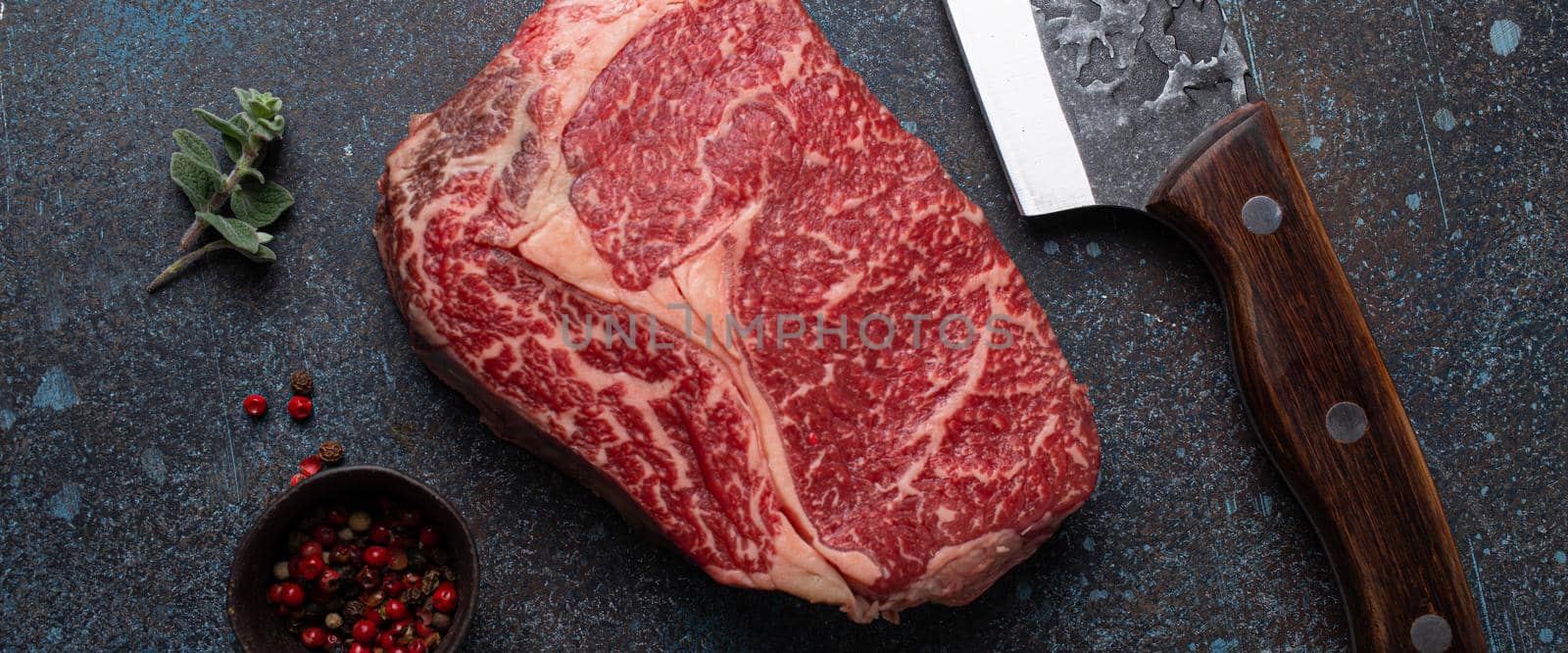 Raw meat beef marbled prime cut steak Ribeye on rustic concrete kitchen table background from above with big knife and spices, beefsteak concept