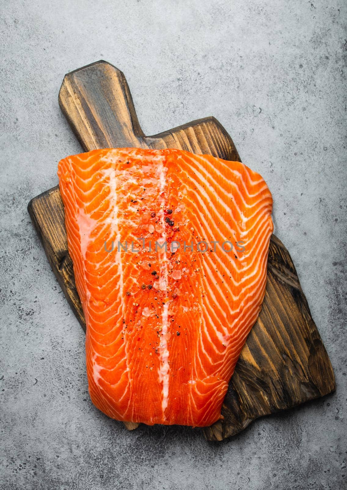 Top view, close-up of whole  fresh raw salmon fillet with seasonings on wooden board, gray stone background. Preparing salmon fillet for cooking, healthy eating concept