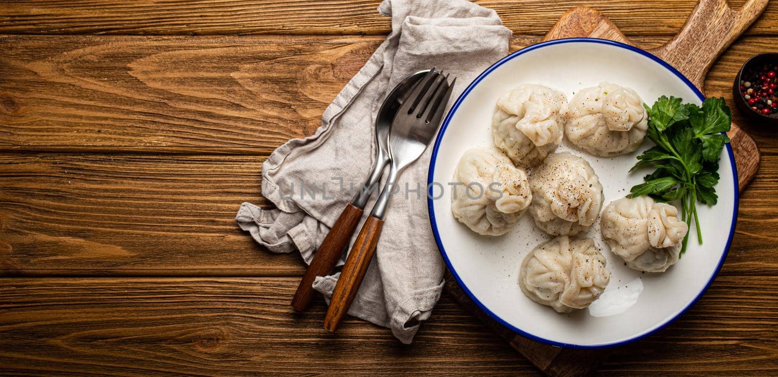 Khinkali, traditional dish of Georgian Caucasian cuisine, dumplings filled with ground meat on white plate with herbs on wooden rustic background table top view space for text.