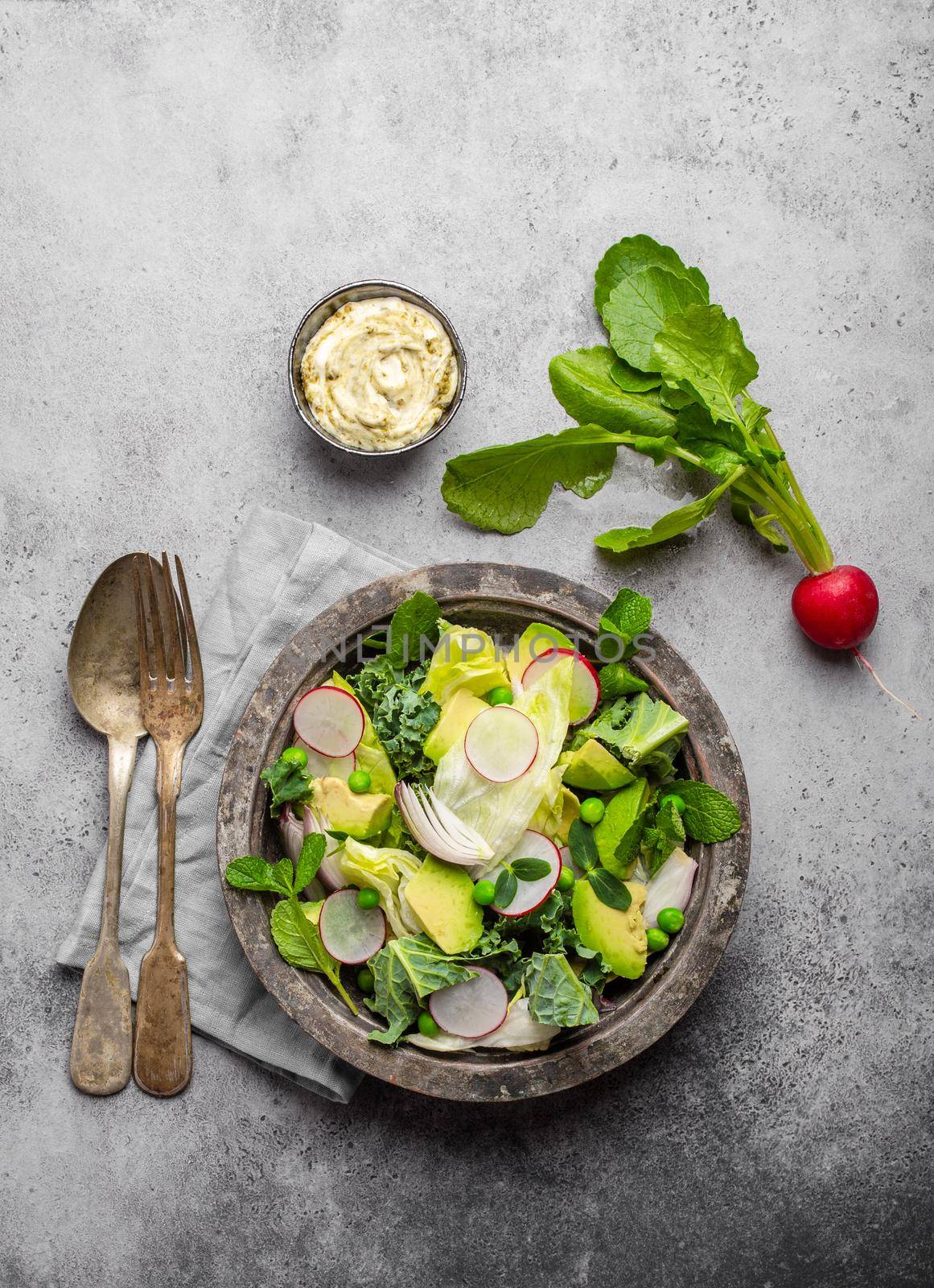 Green organic vegetables salad with avocado, kale, green peas, sprouting herbs in rustic bowl served with sauce, gray concrete background, close-up, top view. Healthy clean eating, diet/detox concept