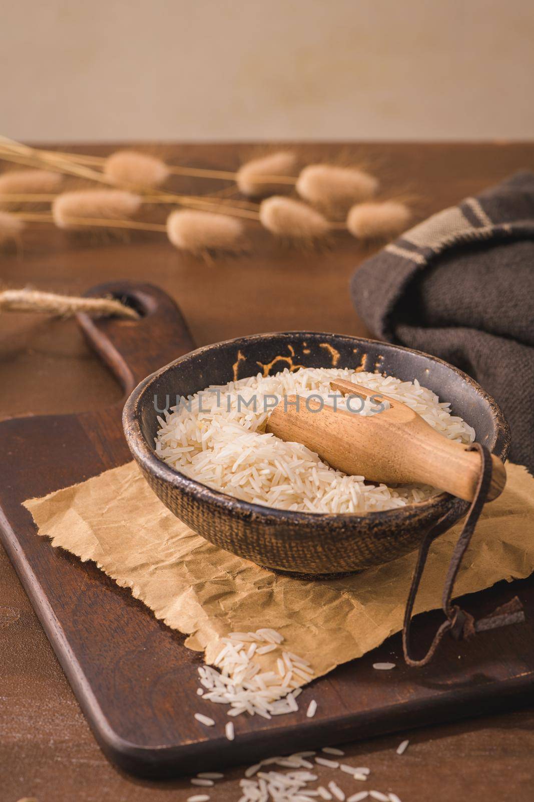 Basmati rice in ceramic bowl with wooden scoop on rustic countertop.