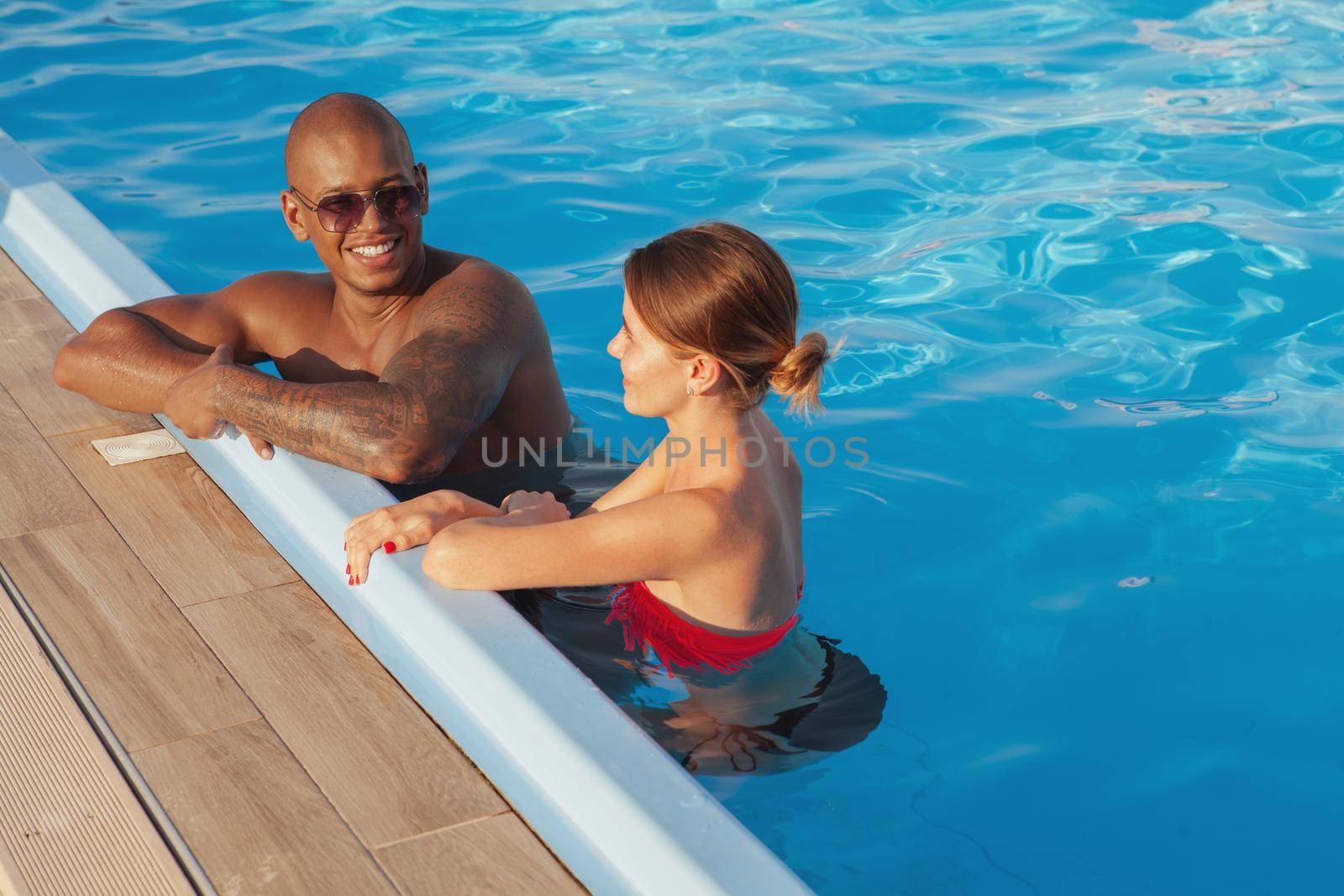 Happy multiethnic couple relaxing in the swimming pool together, copy space. Attractive African man and his girlfriend enjoying summer vacation at seaside resort