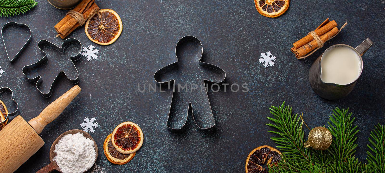 Christmas and New Year baking composition with kitchen tools, flour, milk, balls, fir tree and gingerbread man cutter in center on dark blue stone concrete background table top view