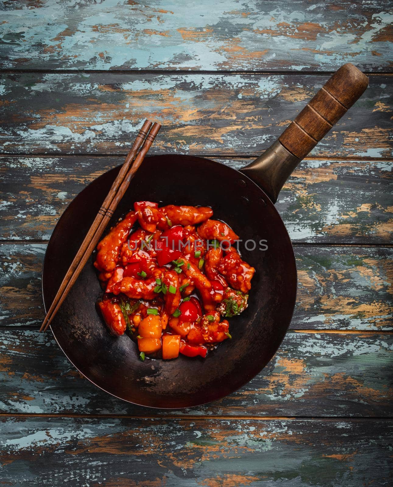 Asian or Chinese style delicious chicken in sweet and sour sauce served in black rustic wok pan on colorful wooden background. Asian dinner concept, top view, close-up