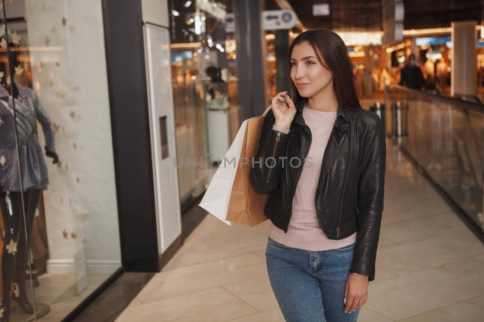 Gorgeous young woman carrying shopping bag while looking at retail display of clothing store