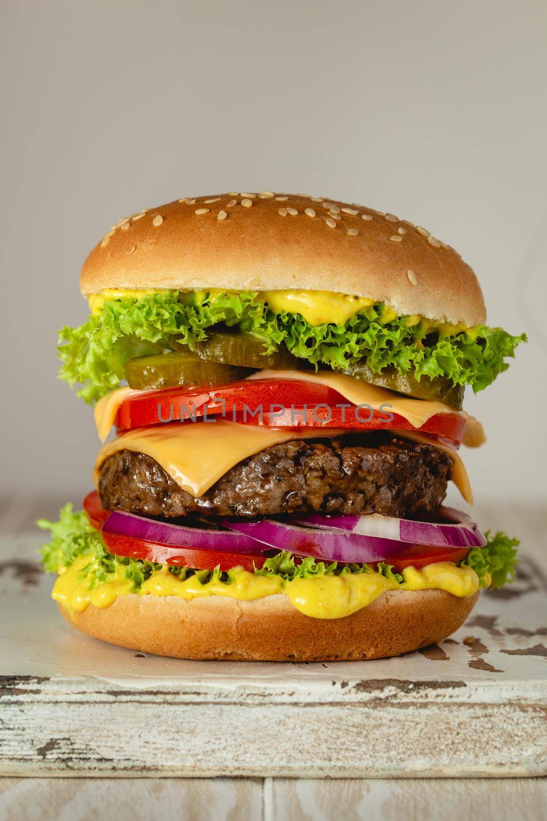 Delicious burger with meat, melted cheese, dripping sauce and vegetables on white rustic background. Freshly made tasty hamburger, close-up.