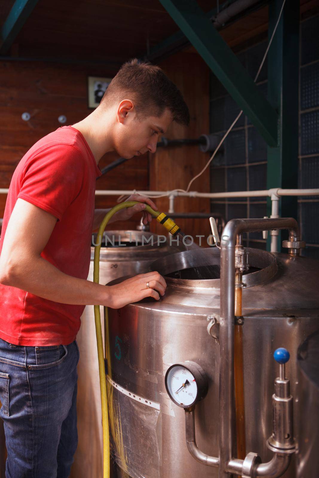 Vertical shot of a brewery employee washing inside metal beer container