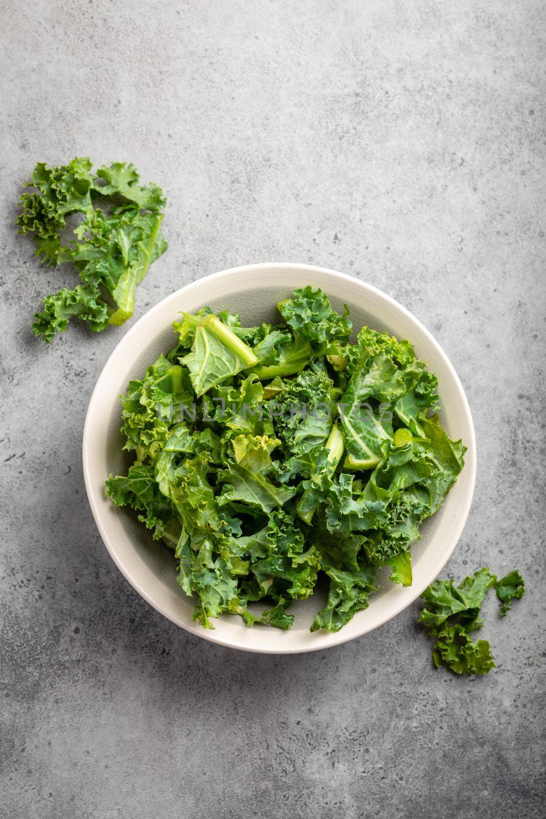 Bowl of fresh green chopped kale on gray rustic stone background, top view, close-up. Ingredient for making healthy salad. Clean eating, detox or diet concept