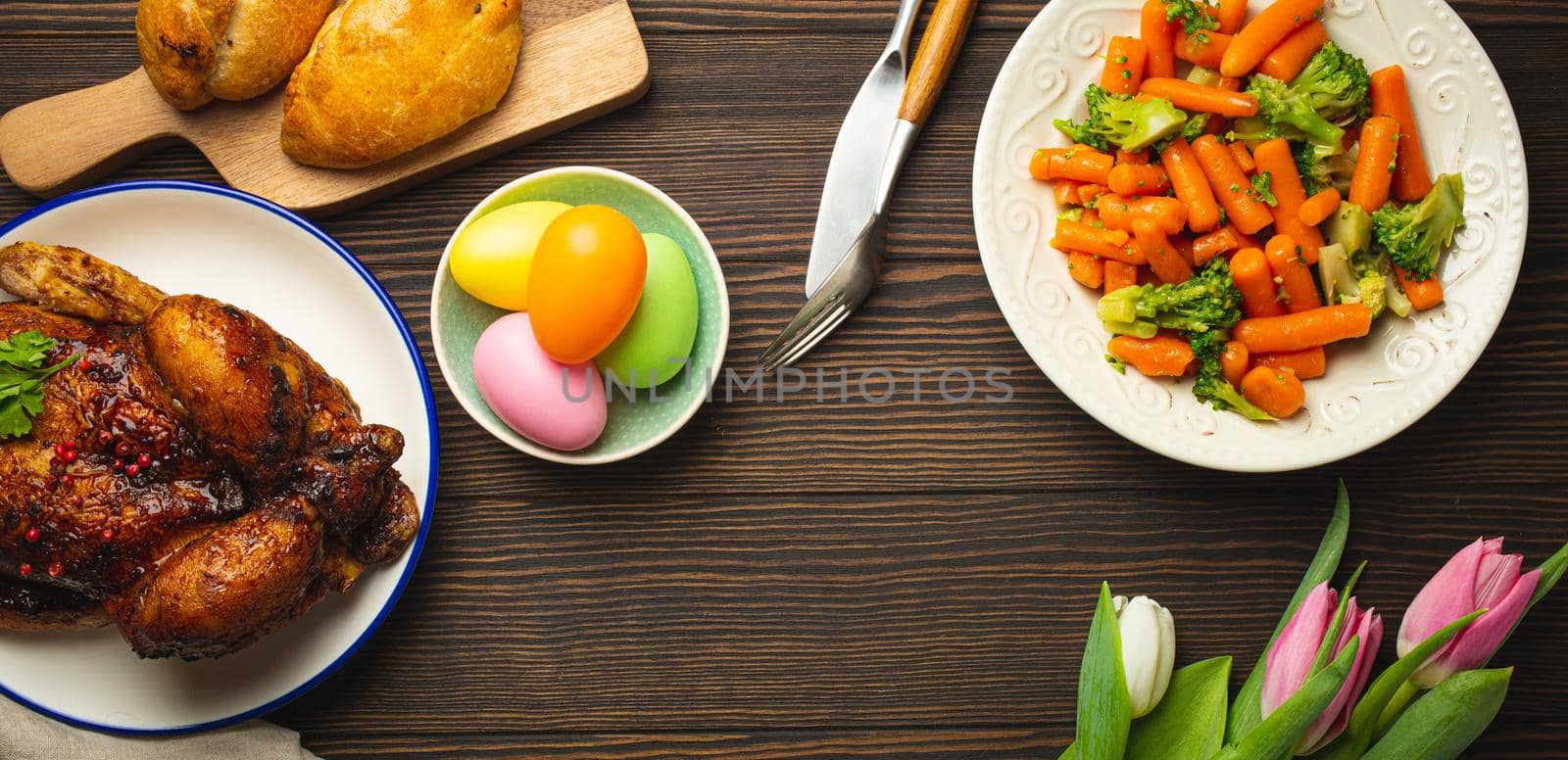 Easter food on dark rustic table: pastel colored eggs, roasted chicken, vegetables, buns by its_al_dente