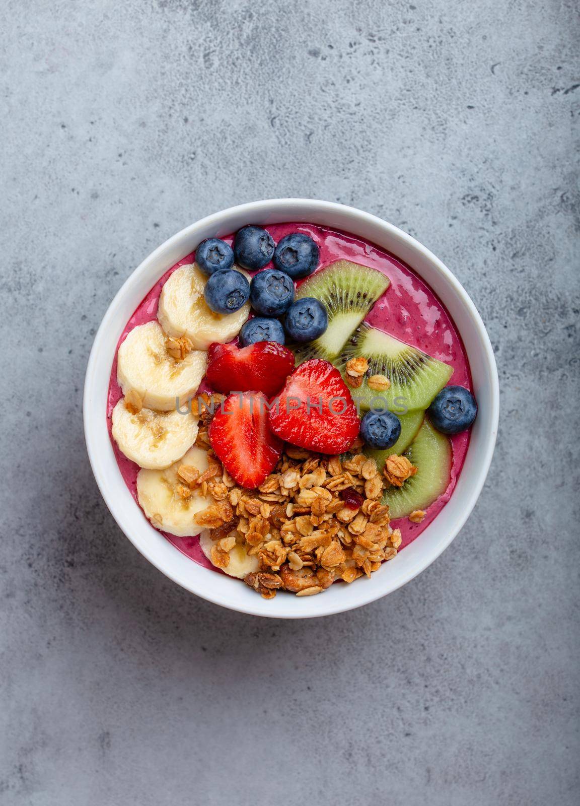 Two summer acai smoothie bowls with strawberries, banana, blueberries, kiwi fruit and granola on gray concrete background. Breakfast bowl with fruit and cereal, close-up, top view, healthy food