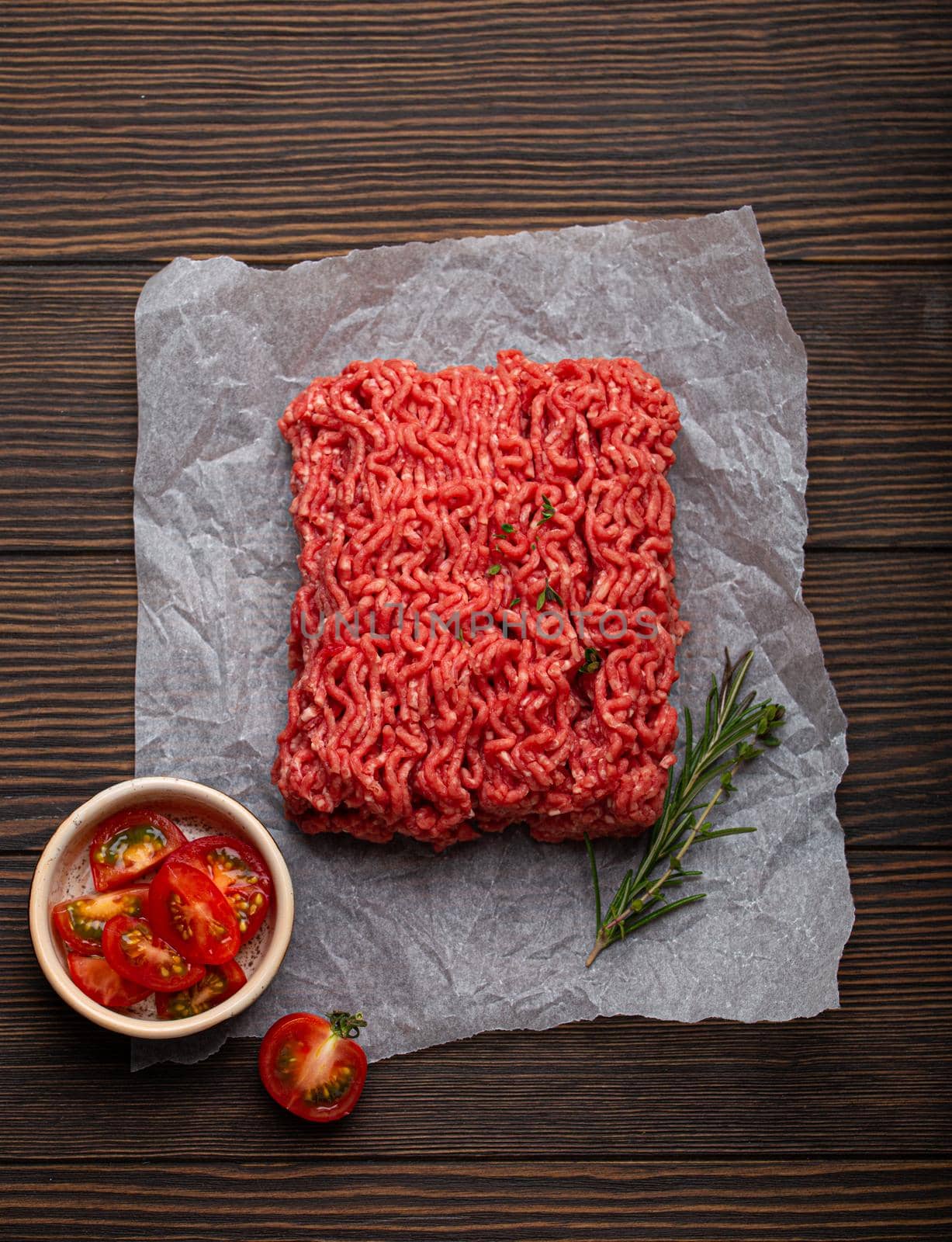 Fresh raw minced meat from ground beef or pork with ingredients for cooking on cutting board and dark brown rustic wooden background from above