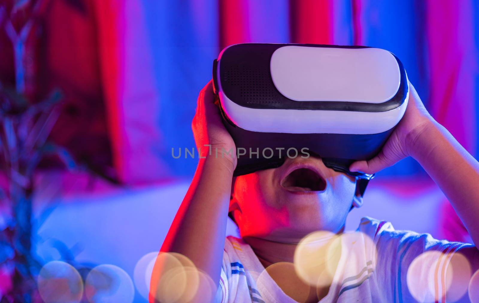 Asian little kid boy wearing virtual reality goggles experiencing reality, Child wear VR helmet excited open mouth at home dark purple and blue background, Virtual technology