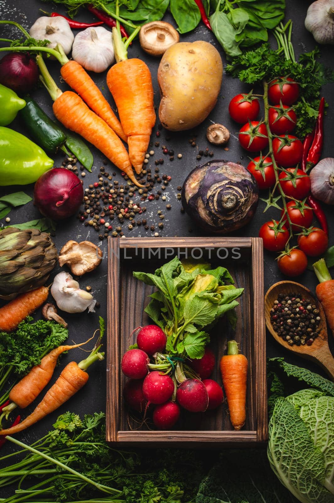 Radish and carrot fresh bunch in old wooden box and fresh farm organic vegetables on rustic black concrete background. Autumn harvest, vegetarian food or clean healthy eating concept, top view