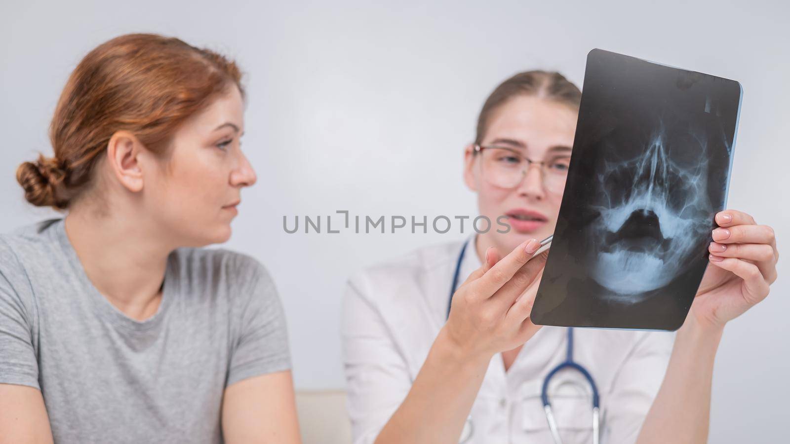 A woman doctor and a patient at the reception are discussing an x-ray of the sinuses. by mrwed54