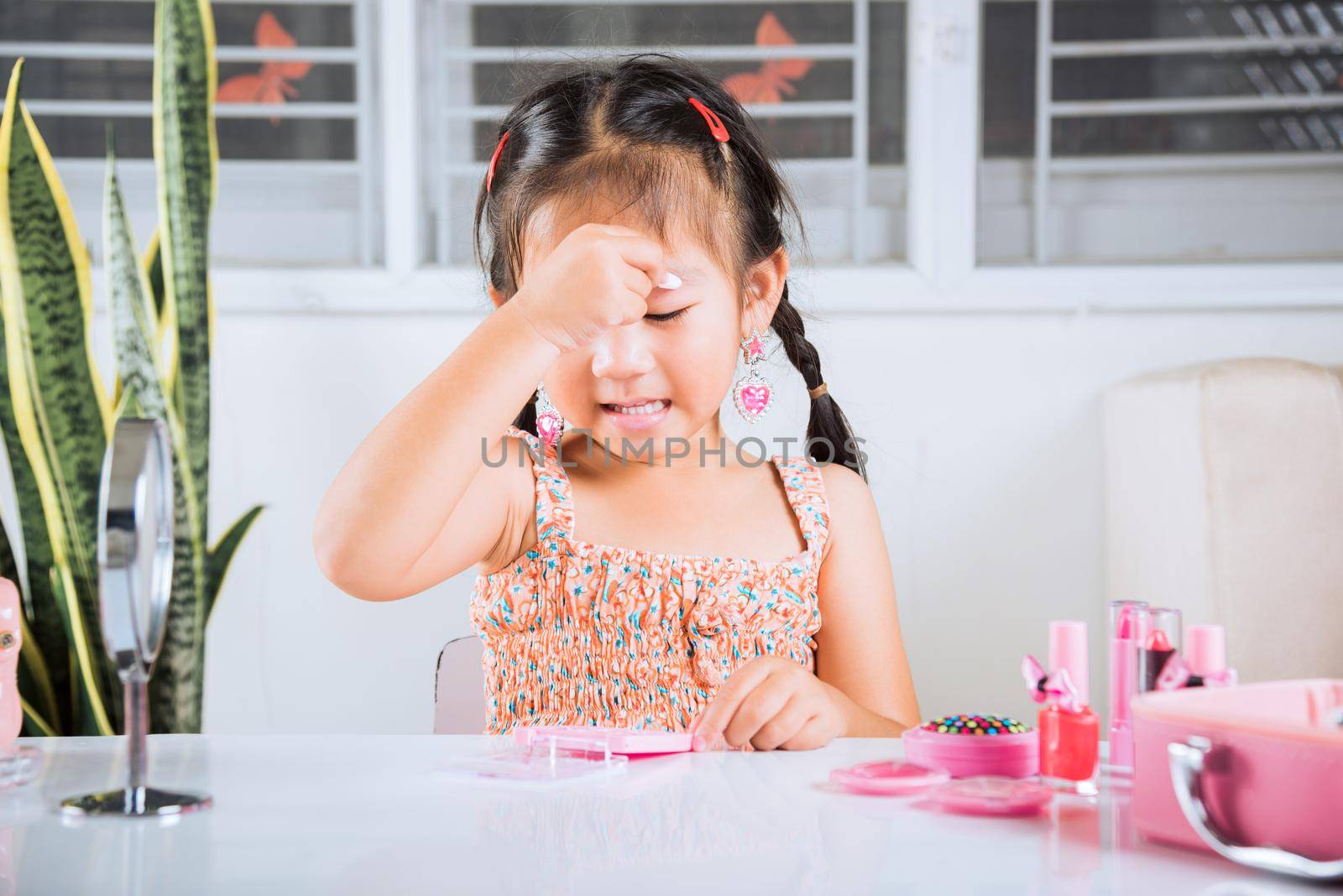 Happy kid is beautiful make up with cosmetics toy, Asian adorable funny little girl making makeup her face she applying carborundum eyeliner to eyelid, Learning activity to be woman at house