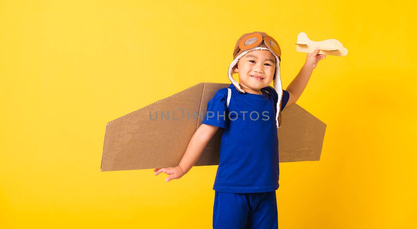 Kid little boy smile wear pilot hat play and goggles with toy cardboard airplane wings by Sorapop