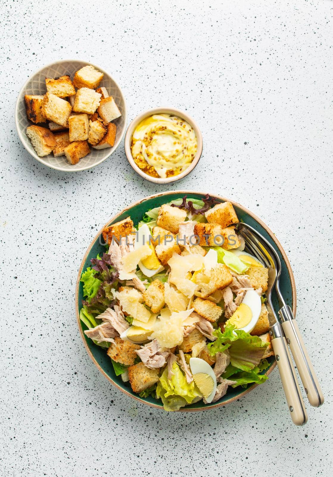 Fresh Caesar salad with lettuce salad, chicken breast, boiled eggs and croutons in ceramic bowl with dressing on the side on white table. Top view, healthy salad great for lunch, snack or appetizer