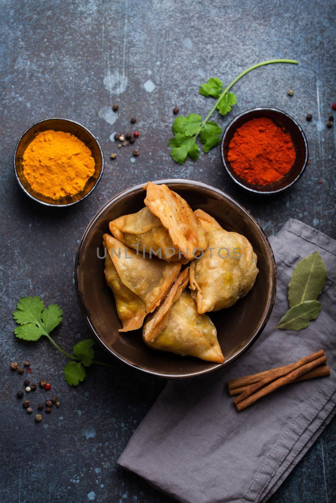 Indian samosas - fried/baked pastry with savoury filling, popular Indian snacks, served in bowl with spices and fresh cilantro on rustic background, top view. Overhead of samosas