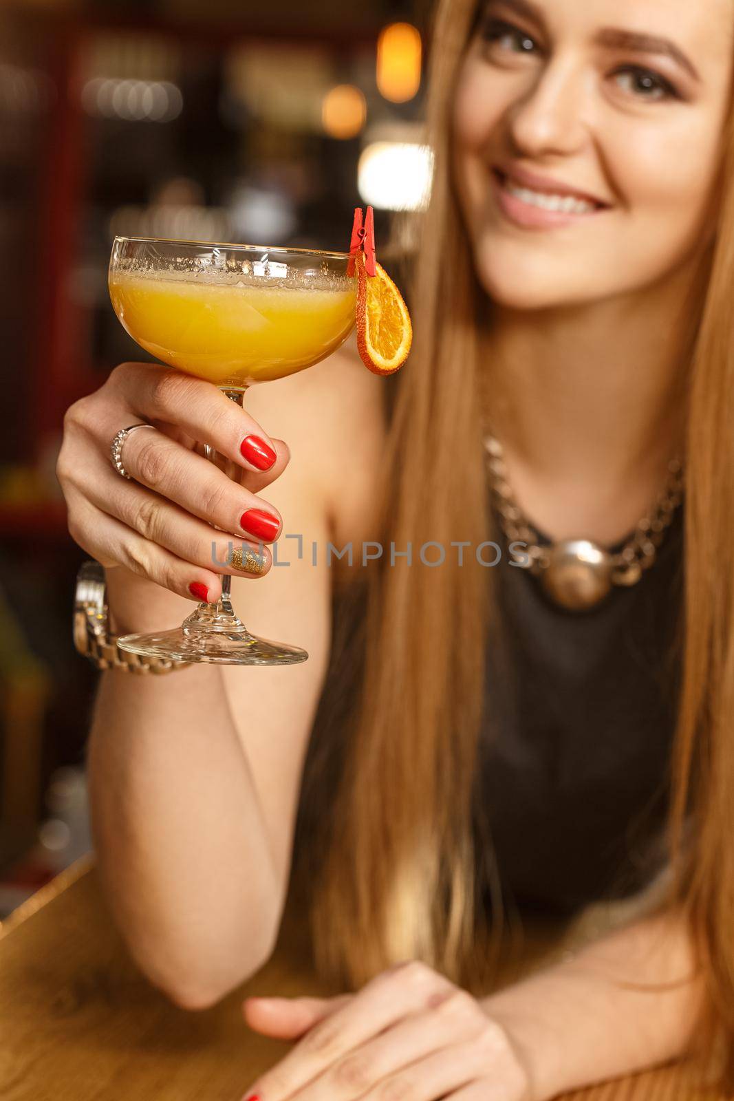 Orange dreams. Selective focus on a cocktail glass in the hands of a beautiful happy woman she is toasting with