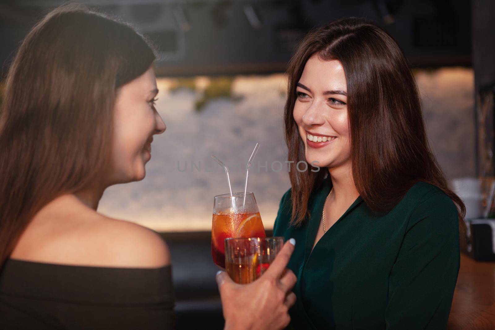 Charming happy woman laughing, talking to her friend at the bar while having cocktails together