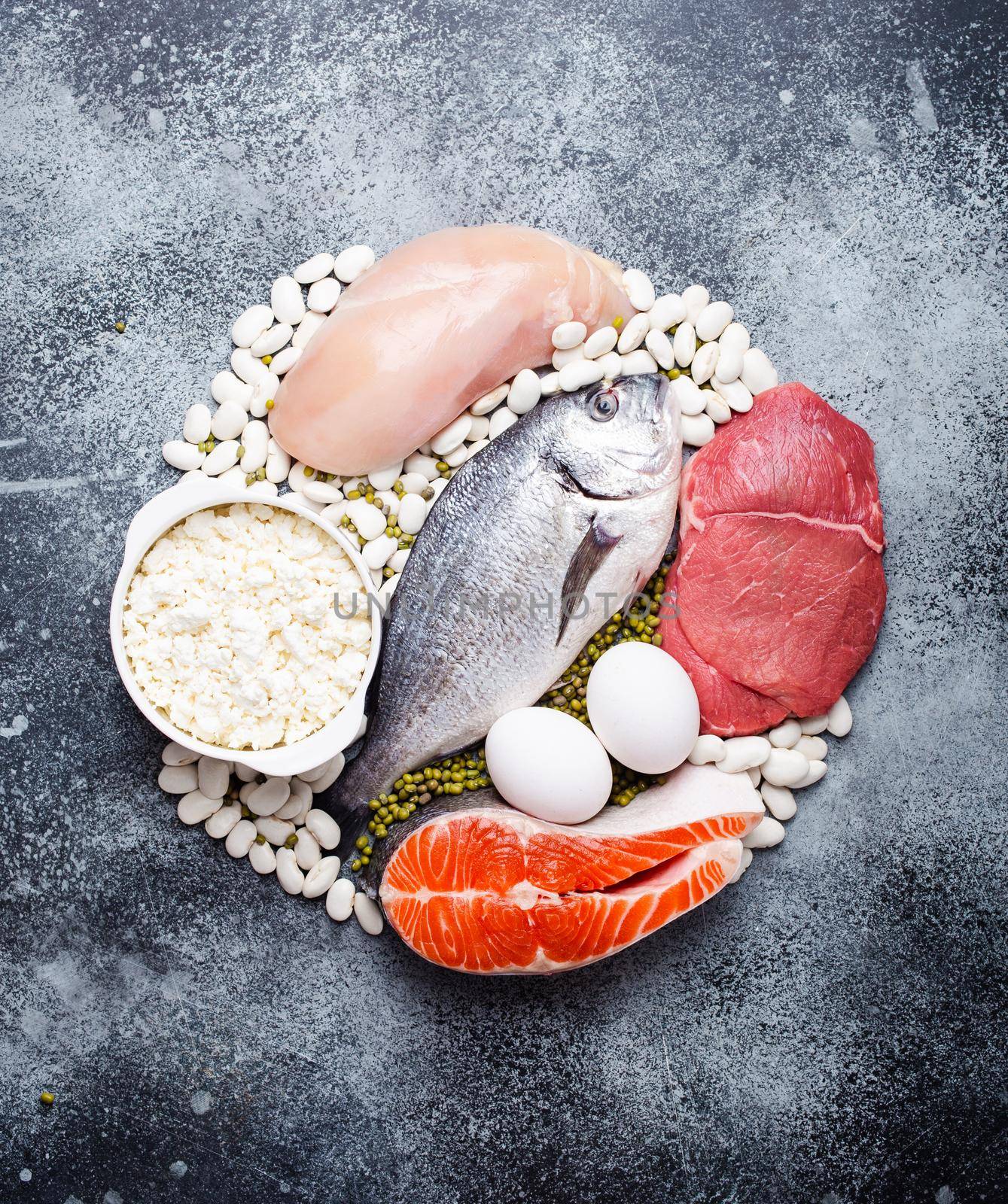 Different types of natural healthy foods contain protein: fish, meat, chicken, eggs, dairy products, beans on gray concrete background, top view, close up. Protein foods for diet and proper nutrition .