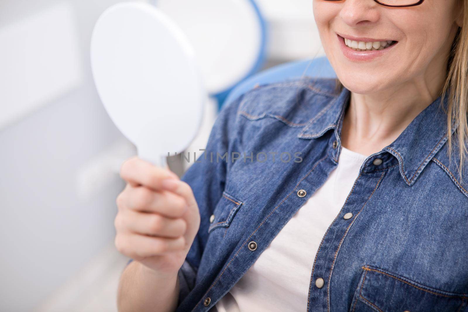 Cropped shot of a female patient examining her teeth in the mirror after dental treatment